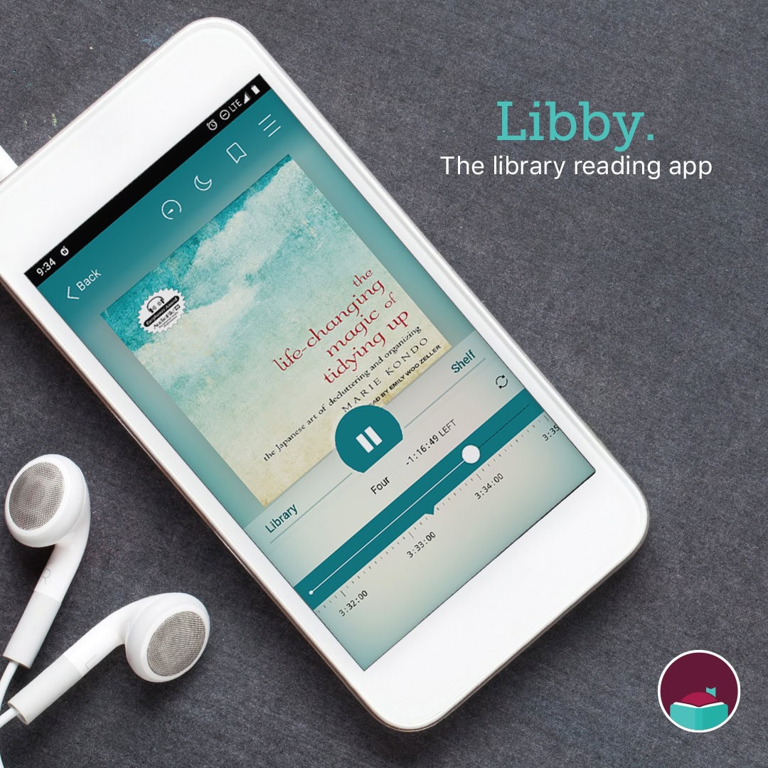 A white smartphone displays the Libby library reading app, playing the audiobook The Life-Changing Magic of Tidying Up. White earphones are beside the phone on a dark surface.