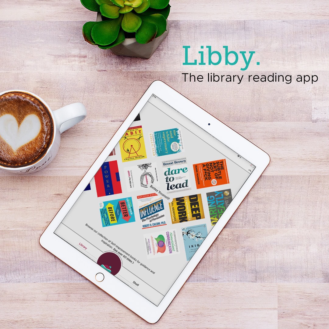 A tablet displaying colorful book covers, next to a cup of coffee with latte art and a small green plant. Text on the wooden table reads Libby. The library reading app.